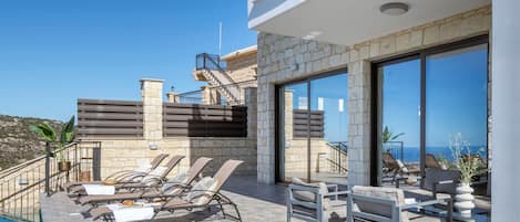 Un área lounge moderna al aire libre con piscina, muros de piedra y vista al mar.