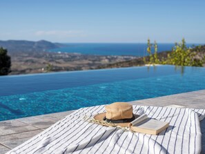 A poolside area with a hat, book, and straw on a striped towel. - Sea-view Retreat - Villas With Private Pools (Peristerona)