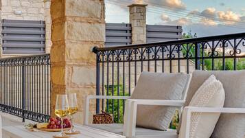 A balcony with a stone wall, a white table with a glass of wine, a wicker basket, and a white sofa with cushions.