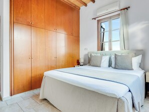 Un dormitorio con un amplio armario de madera, una cama con muchos cojines y una ventana con cortinas.