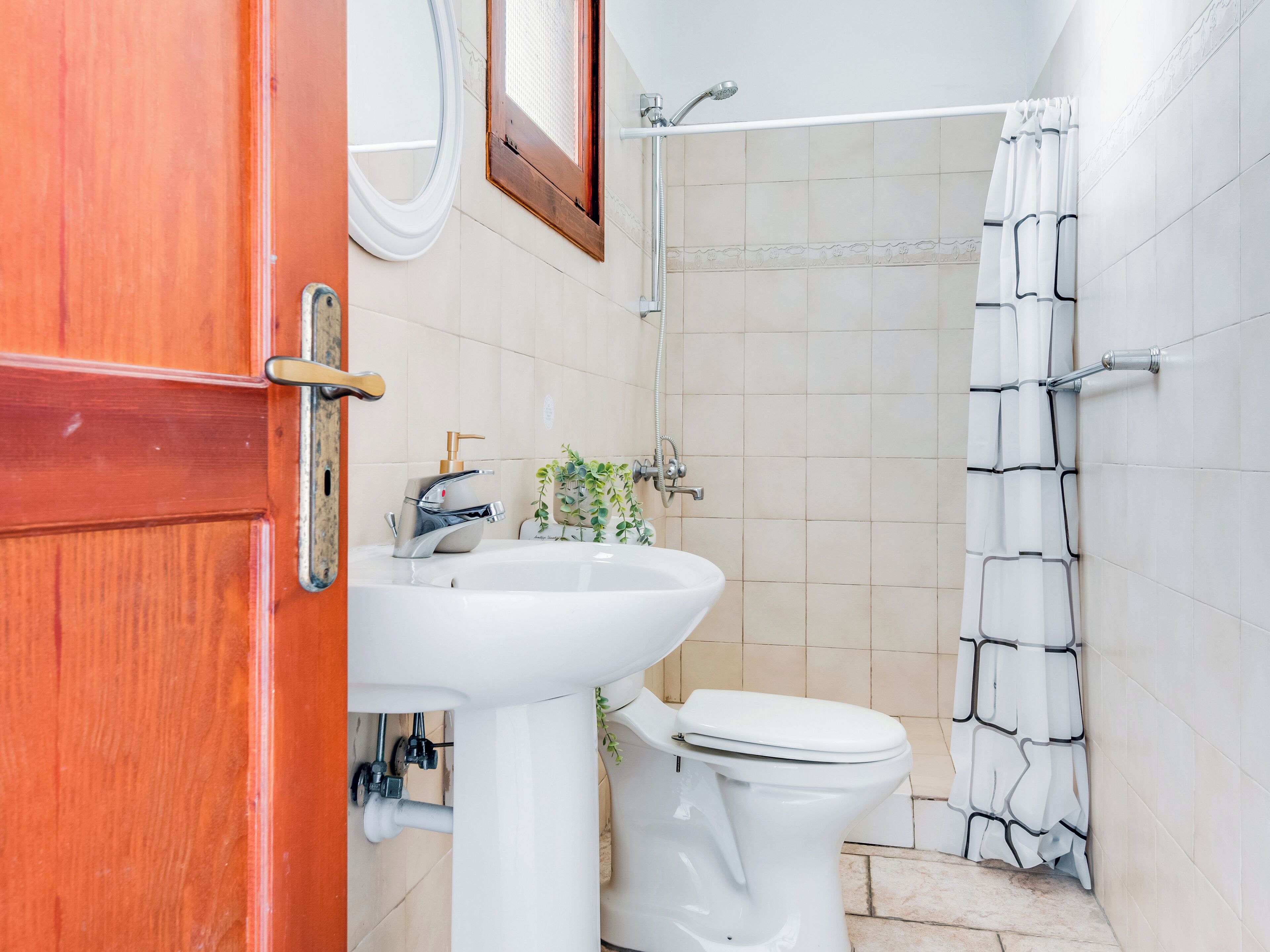 A bathroom with a sink, toilet, shower, and a wooden door.