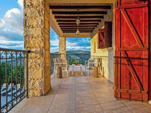 A balcony with stone pillars, a red door, and two white chairs with cushions.