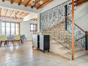 Una habitación amplia con comedor, una escalera con barandales de metal ornamentados y techo de madera.