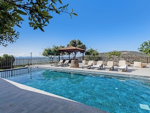 A clear blue pool with lounge chairs and a gazebo.