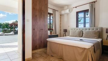 A bedroom with a bed, a wooden wardrobe, an air conditioning unit, a window with curtains, and a view of an outdoor area.