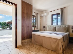 A bedroom with a bed, a wooden wardrobe, an air conditioning unit, a window with curtains, and a view of an outdoor area.