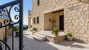 A stone building with a sign reading 'ALEXANAROS PALACE,' a gated entrance, and potted plants on the steps.