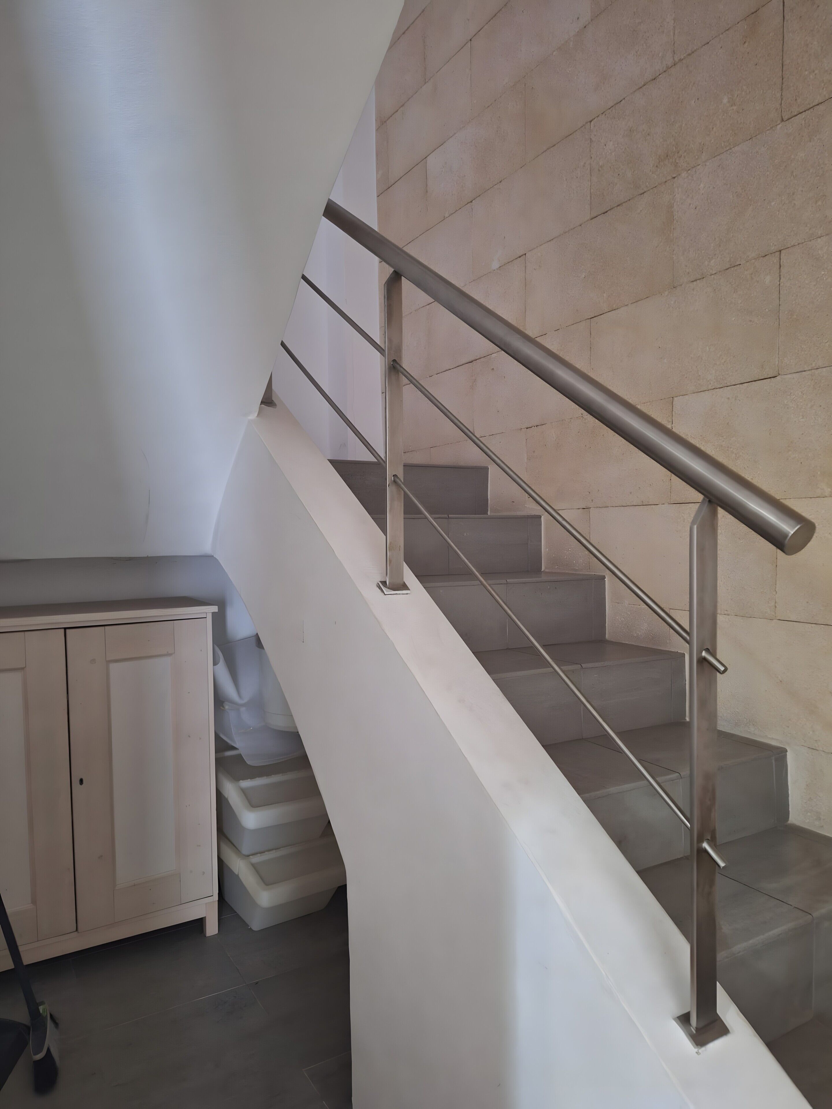 Uma escadaria moderna com corrimão de metal, parede branca e armário de madeira.