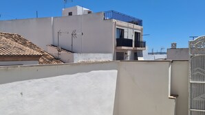 Una terraza en la azotea con un muro blanco, una verja de metal y un edificio con balcones al fondo.