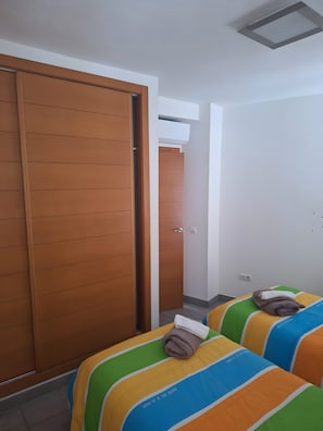 A hotel room with a wooden wardrobe, a bed with colorful bedding, and an air conditioning unit on the wall. - Casa Roques Old Town Xabia (Xàbia)
