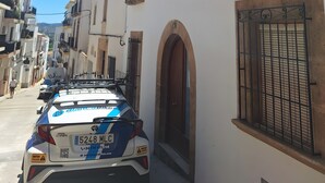 Una calle estrecha con edificios blancos, un coche aparcado y un cielo azul despejado.