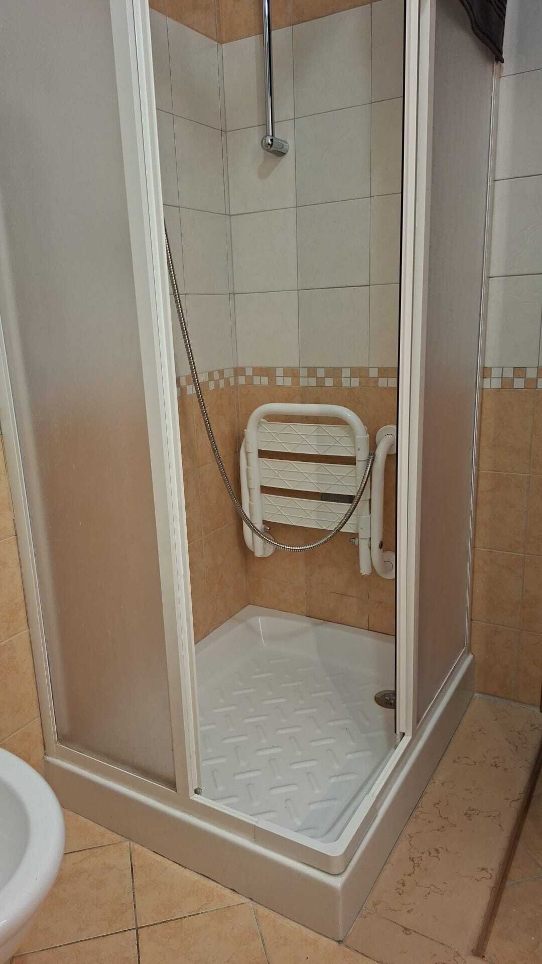 A shower with a glass door, a white shower seat, and a tiled floor.
