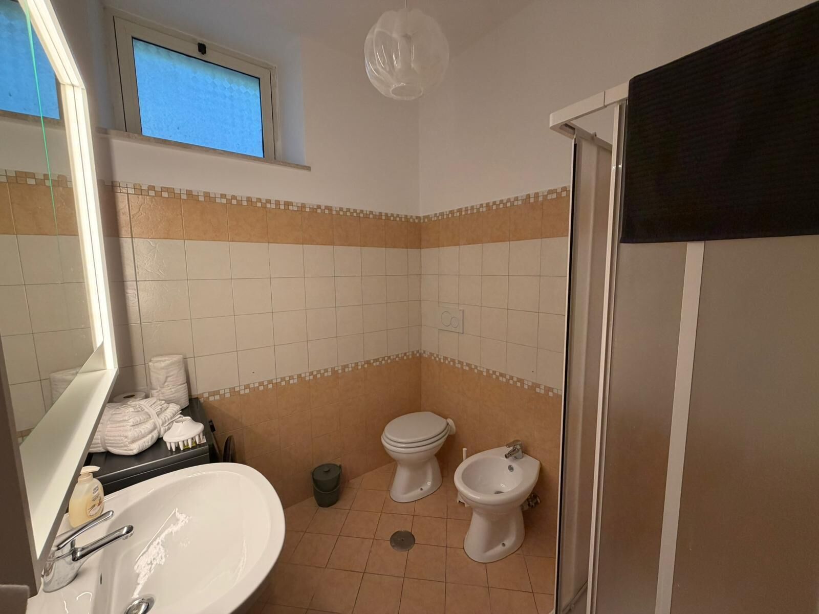 A bathroom with a sink, toilet, bidet, and a window above the toilet.