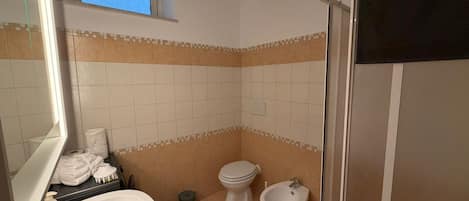 A bathroom with a sink, toilet, bidet, and a window above the toilet.