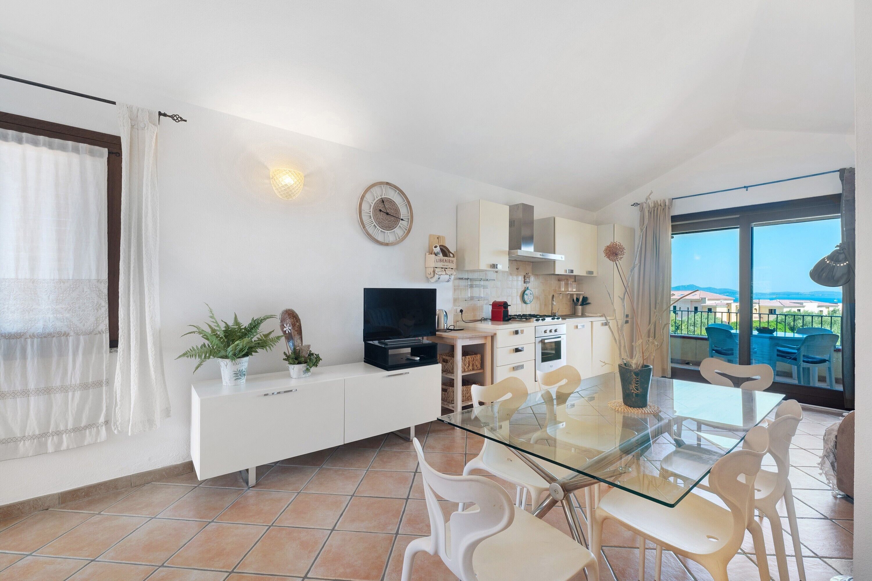 A modern kitchen with a dining area, a TV, and a view of the sea.