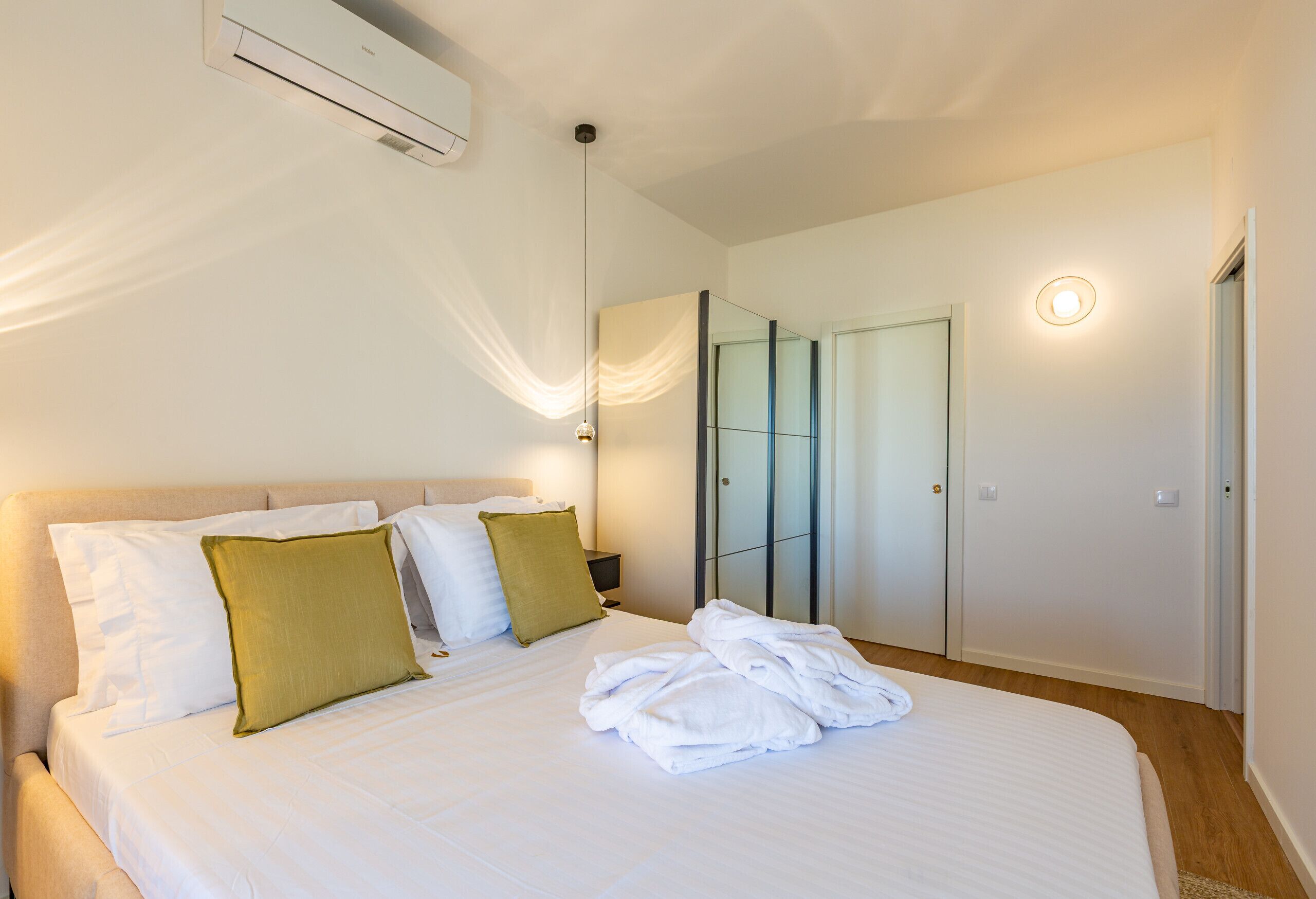 A bedroom with a bed, pillows, a bedside table, a mirror, and a wardrobe.
