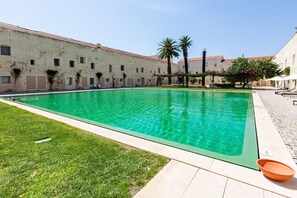 Una piscina con agua cristalina, rodeada de césped y un edificio con varias ventanas y puertas.