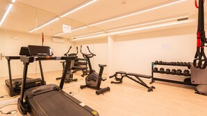 Et træningscenter med løbebånd, crosstrainer, bænk og et stativ med håndvægte.