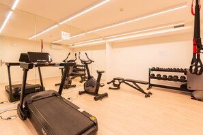 Ein Fitnessraum mit Laufbändern, einem Crosstrainer, einer Trainingsbank und einer Hantelbank.