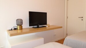Et værelse med et fladskærms-tv på en træhylde, en lampe og et hvidt natbord.