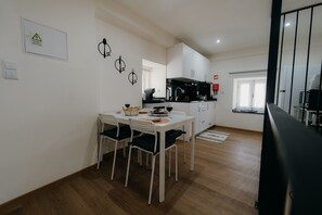 A modern kitchen with white cabinets, a dining table with four chairs, and a black countertop. - Casa Santana - Uva Douro Houses (Casais do Douro)