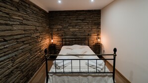 A bedroom with a stone wall, a metal bed frame, and two bedside lamps. - Casa de Xisto - Uva Douro Houses (Ervedosa do Douro)