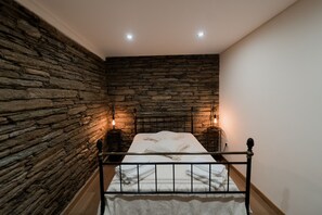 A bedroom with a stone wall, a metal bed frame, and two bedside lamps. - Casa de Xisto - Uva Douro Houses (Ervedosa do Douro)
