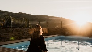 A person seated by a pool with a view of a mountainous landscape and a fence. - Casa de Xisto - Uva Douro Houses (Ervedosa do Douro)