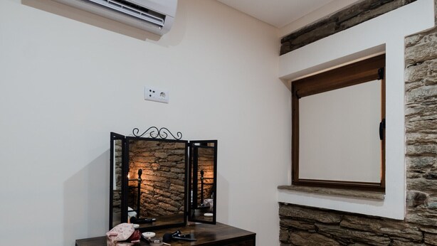 A room with a wooden vanity, a mirror, a stone accent wall, and a white air conditioning unit mounted on the wall. - Casa de Xisto - Uva Douro Houses (Ervedosa do Douro)