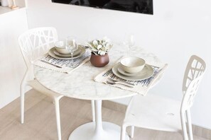A round table with white chairs, a small potted plant, and a placemat.