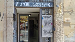 Liiketila, jonka edessä on kyltti, jossa lukee ”AlterCAD Copisteria Stampa Digitale”, ja jossa on lueteltu tarjolla olevia palveluita, kuten kopiointi ja tulostus.