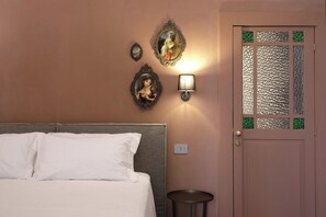 A bedroom with a bed, a wall-mounted lamp, two decorative mirrors, and a door with a textured glass panel. - Charming Suite with Original Frescoes – Exclusive Suite Just 5 Minutes from Ortigia. (Siracusa)