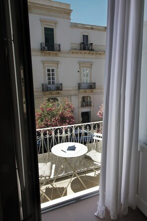 A balcony with a table and chairs, a view of a building with balconies, and a car parked below. - Charming Suite with Original Frescoes – Exclusive Suite Just 5 Minutes from Ortigia. (Siracusa)