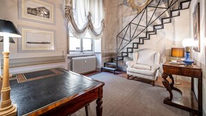 A room with a marble staircase, a white armchair, a wooden table, and framed architectural drawings on the walls. - Vigna Vecchia (Florence)