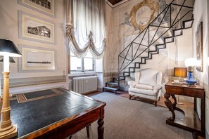 Ein Zimmer mit einer Marmortreppe, einem weißen Sessel, einem Holztisch und gerahmten architektonischen Zeichnungen an den Wänden.