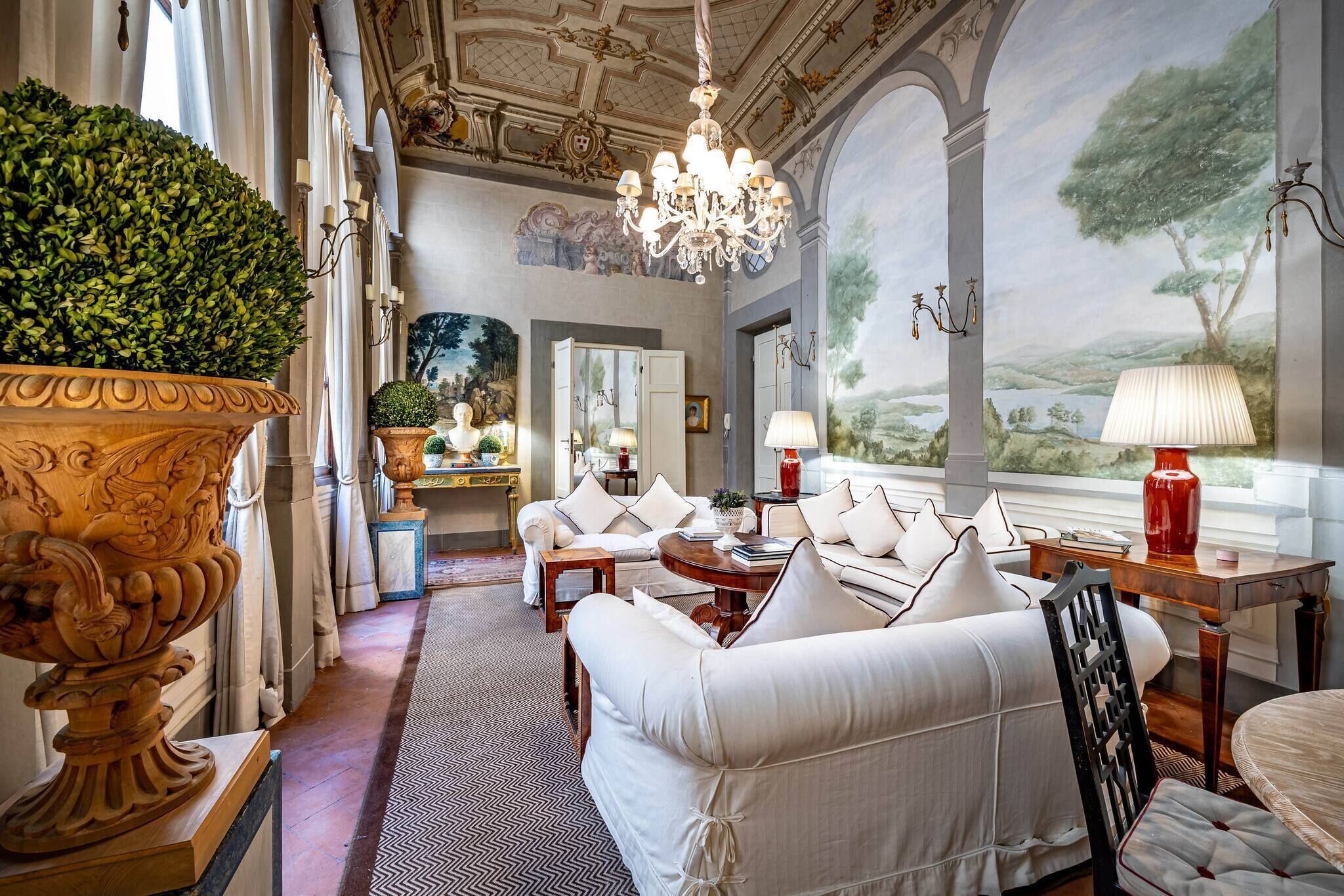 A luxurious room with a large ornate vase, a chandelier, and a scenic mural on the wall.