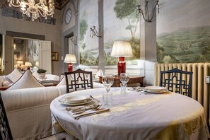 Ein Essbereich mit Tisch, gedeckt für vier Personen, inklusive Teller, Besteck und Gläsern. Zwei Stühle, eine Chandelier und ein großes Landschaftsbild an der Wand sind ebenfalls vorhanden.