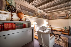 Ein Zimmer mit Schreibtisch, Büchern, Lampe, einer Couch und einer dekorativen Decke.