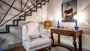 A staircase with a geometric design, a white armchair with a striped pillow, a wooden console table with blue lamps, and a framed portrait on the wall. - Vigna Vecchia (Florence)