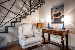 Eine Treppe mit geometrischem Design, ein weißer Sessel mit gestreiftem Kissen, ein Holzkonsole mit blauen Lampen und ein gerahmtes Porträt an der Wand.