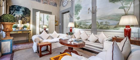 A luxurious living room with a sofa set, a round wooden coffee table, and a large window with a scenic view.