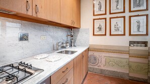 A kitchen with wooden cabinets, a marble countertop, a gas stove, and a sink. There are framed artworks on the wall. - Vigna Vecchia (Florence)