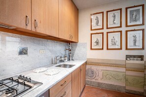 Eine Küche mit Holdekor, einer Marmorarbeitsplatte, einem Gasherd und einem Spülbecken. An der Wand hängen gerahmte Kunstwerke.