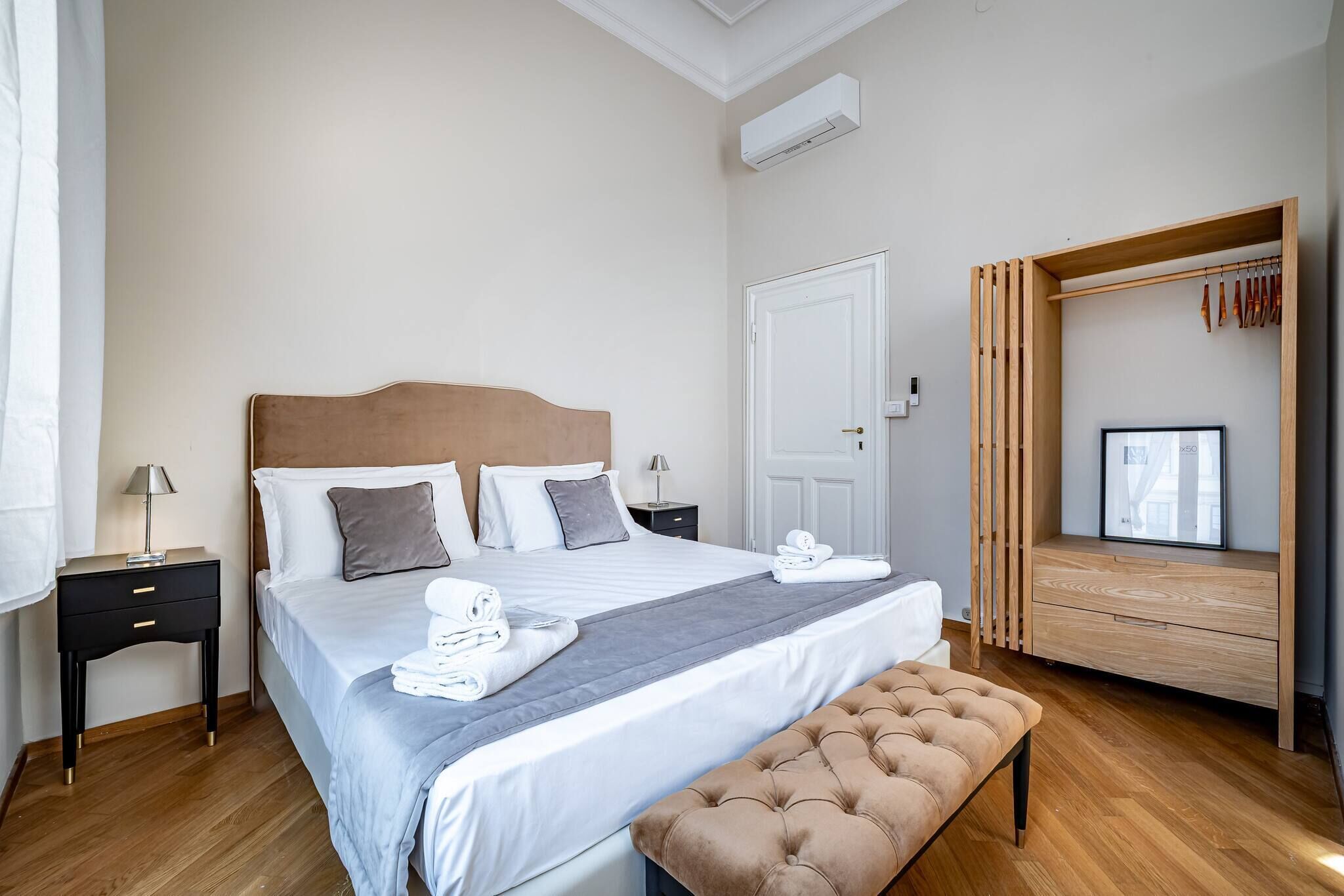 A neatly arranged hotel room with a bed, bedside tables, a bench, a wardrobe, and a window with a view.