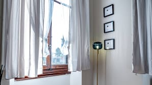 A room with a wooden floor, a black table with a brass bowl, a floor lamp, and a window with curtains. - Poggi 22 (Florence)