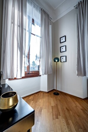 A room with a wooden floor, a black table with a brass bowl, a floor lamp, and a window with curtains. - Poggi 22 (Florence)
