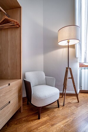 A room with a wooden wardrobe, a grey armchair, a floor lamp, and a radiator. - Poggi 22 (Florence)