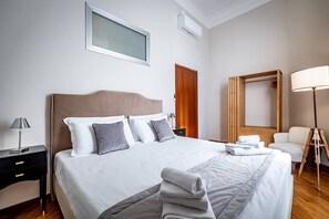Ein ordentlich eingerichtetes Hotelzimmer mit einem großen Bett, einem Nachttisch mit Lampe, einem Holzschrank, einem Spiegel und einer Stehlampe.