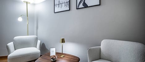 Una habitación moderna con dos sillones grises, una mesa de centro de madera, una lámpara de pie y dos obras de arte enmarcadas en la pared.
