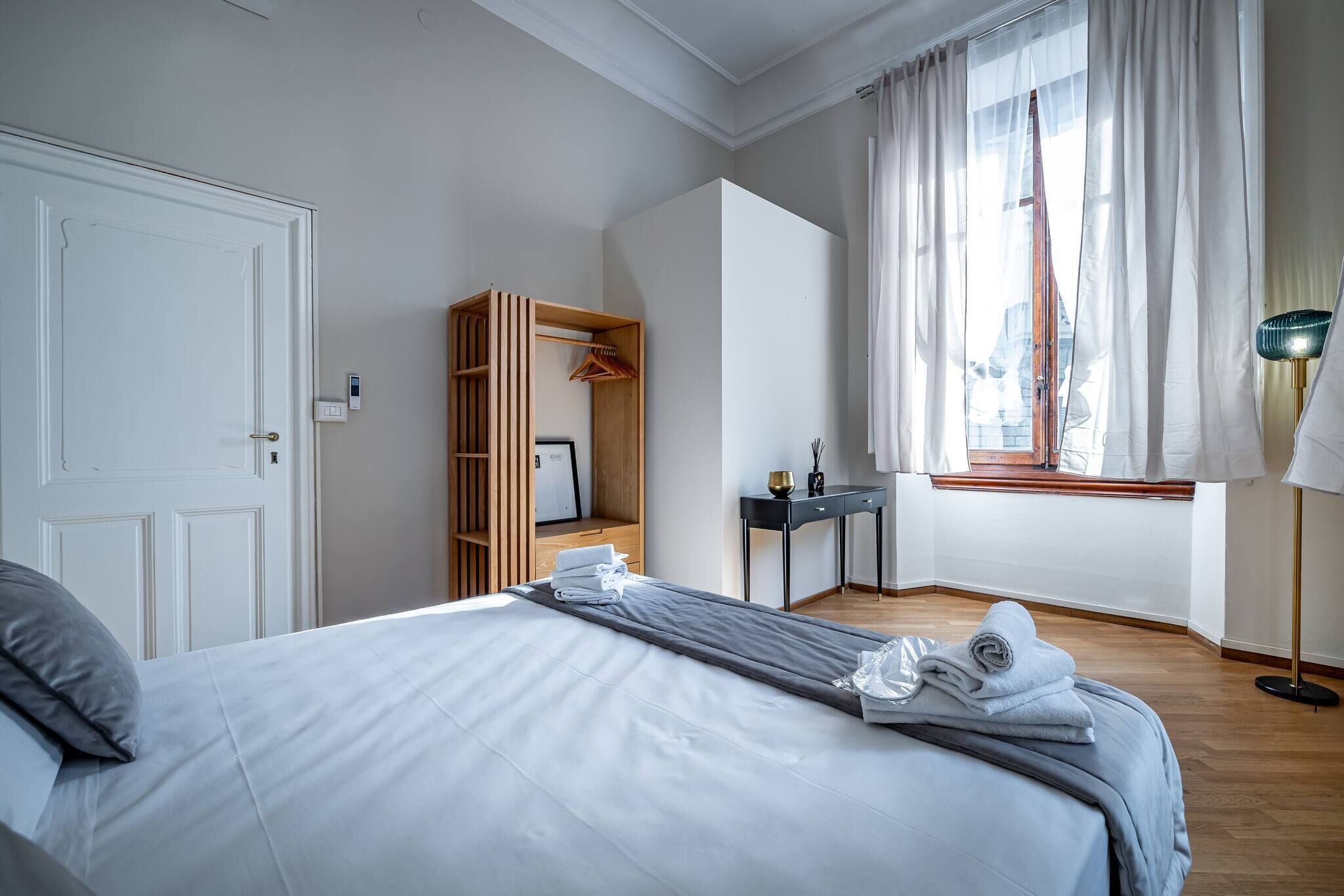 Una habitación de hotel con cama, armario, escritorio y ventana con cortinas.